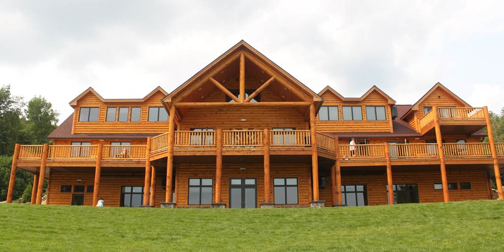 Pine log siding, cedar posts, classic cedar log railing, and milled log truss for Camp Walden summer camp building.