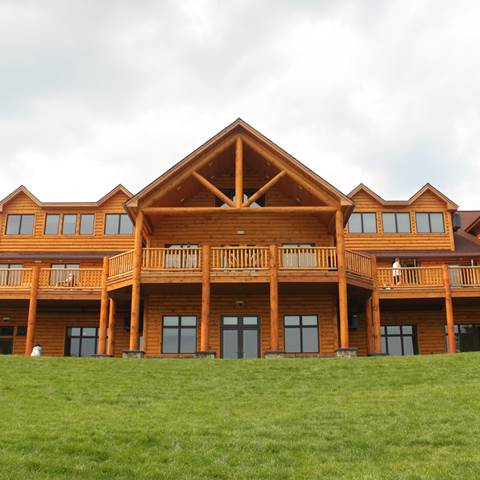 Pine log siding, cedar posts, classic cedar log railing, and milled log truss for Camp Walden summer camp building.