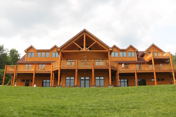 Pine log siding, cedar posts, classic cedar log railing, and milled log truss for Camp Walden summer camp building.